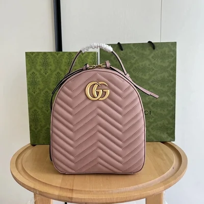 A pink quilted leather backpack with a chevron stitched pattern and a metal clasp, standing on a wooden stool