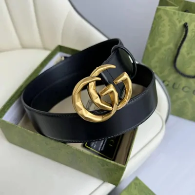 A black leather belt coiled inside its presentation box, with a gold interlocking double ring buckle