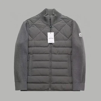A grey quilted down jacket with ribbed knit sleeves and a stand collar, on a plain grey background