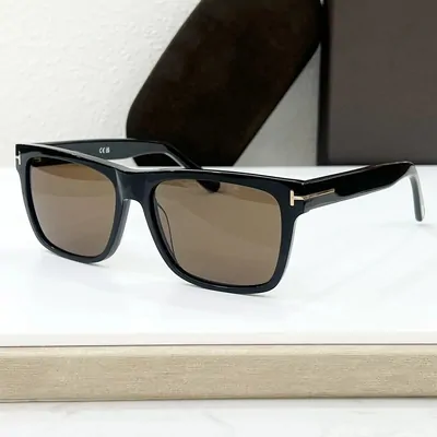 Black rectangular framed sunglasses with brown tinted lenses, resting on a display block