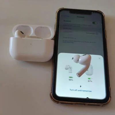 In ear earphones beside their open charging case, with a phone screen showing the battery level of each earpiece