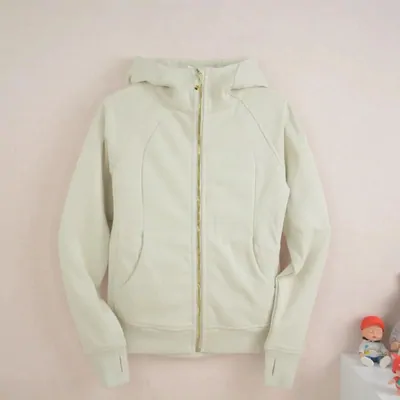 A cream coloured zip up hooded sweatshirt laid flat against a plain backdrop