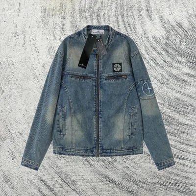 A washed blue denim jacket laid flat on a mottled grey surface, with a hang tag on the chest