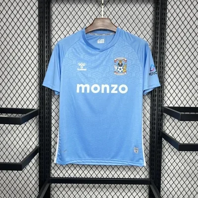 A light blue short sleeved football shirt on a wooden hanger against a black mesh wall