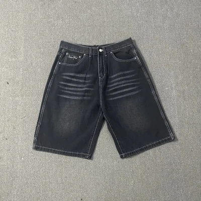 A pair of dark washed denim shorts laid flat on a grey concrete surface