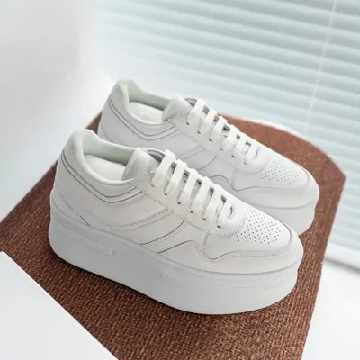 A pair of white leather platform sneakers with perforated toe panels, placed on a pale surface